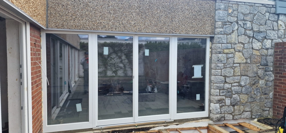 Fenstermontage: weiße Kunststoff-Schiebetür mit vier Elementen in Fassadenöffnung, unvollständiger Terrassenboden