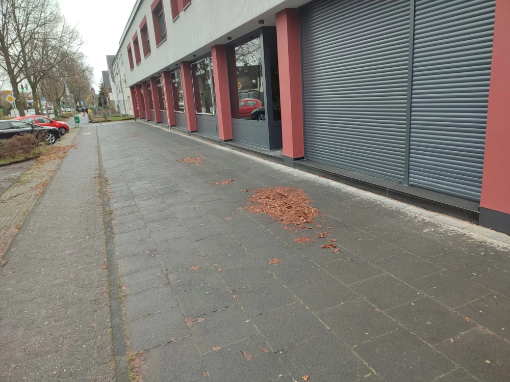 Rote Fassade mit geschlossenen Rollläden und breitem Bürgersteig
