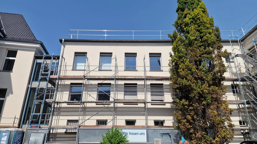 Mehrstöckige Hausfassade mit montiertem Gerüst und ungestrichener Putz für Fassadensanierung