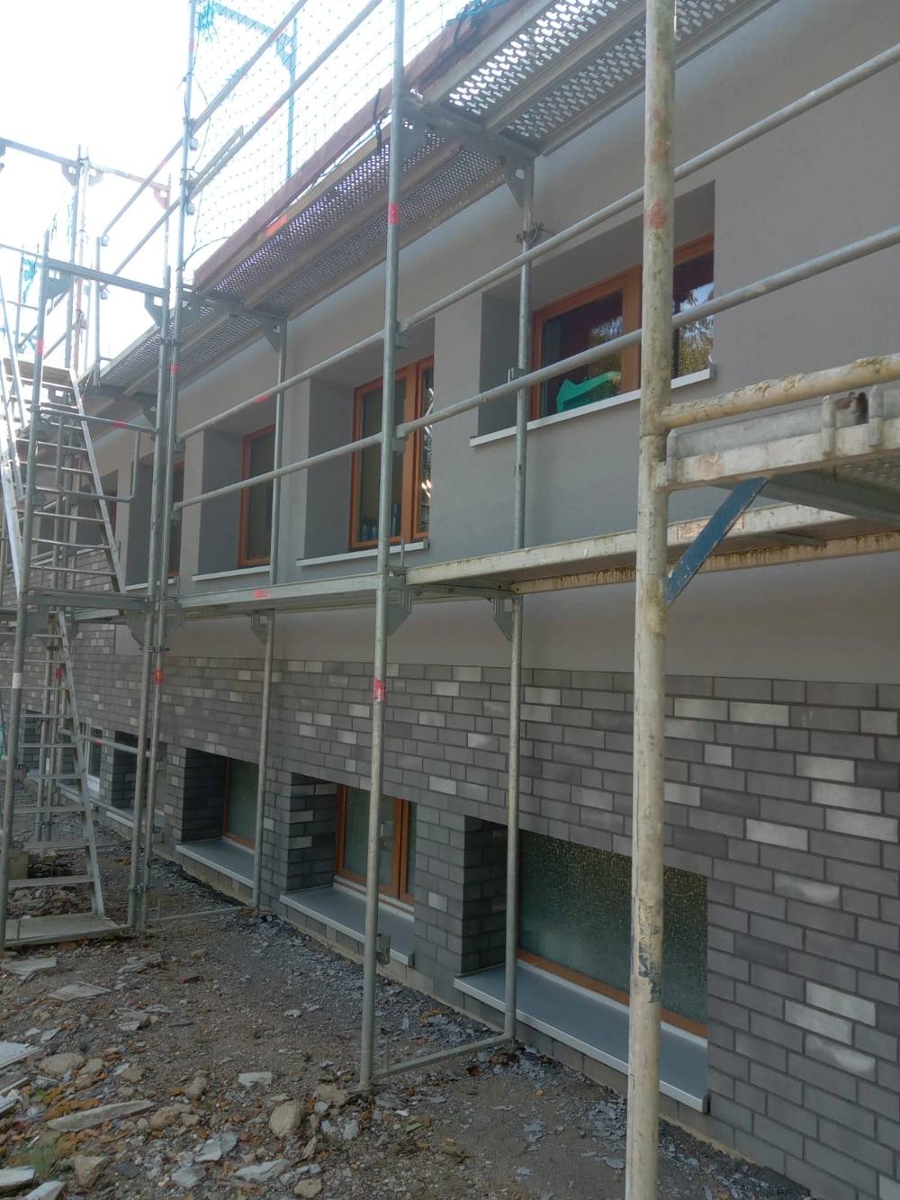 Gerüst vor Hausfassade mit grauen Klinkern und Holzfenstern im Rahmen der Fassadensanierung