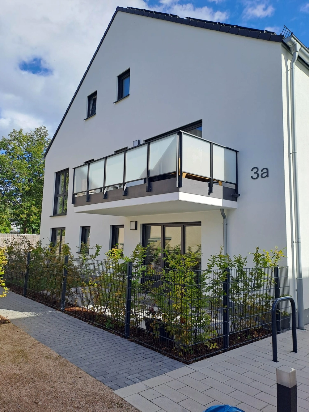 Moderne weiße Außenputzfassade mit Balkon, dunklen Fensterrahmen und Metallzaun Außenputz