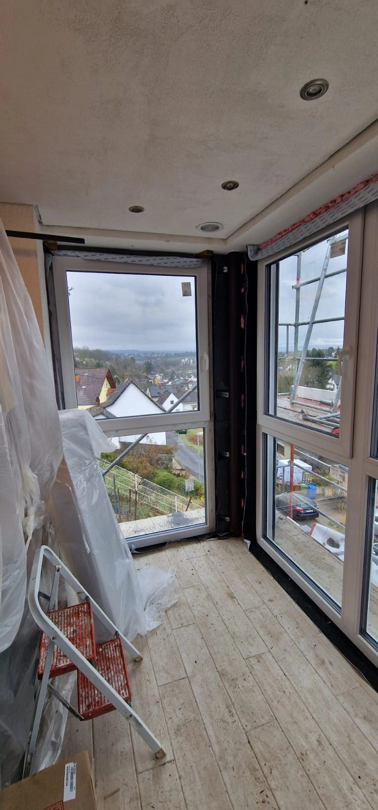 Innenansicht eines Raums mit neuer Fenstermontage, Schutzfolie, Leiter und Ausblick durch großflächige Verglasung