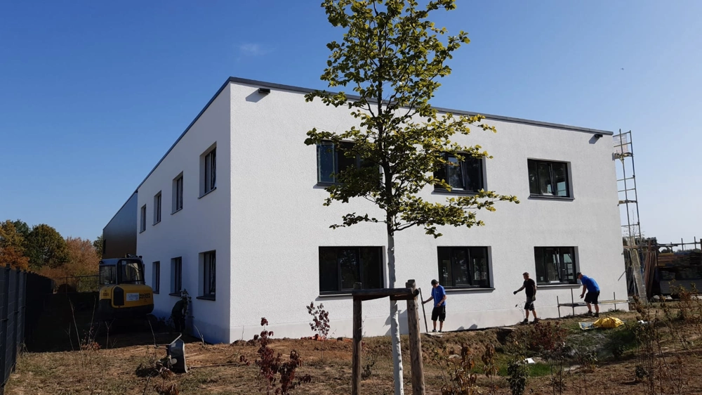 Arbeiter tragen weißen Außenputz an zweigeschossige Fassade eines Neubaus auf