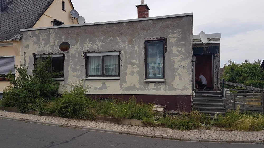 Abgeblätterte Außenfassade mit Fenstern und Haustür, sichtbar schadhafter Putz für Fassadensanierung