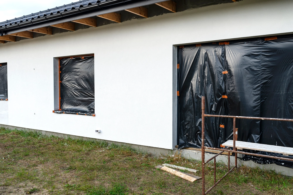 Weiße Fassade mit frischem Außenputz und abgeklebten Fenster- und Türöffnungen