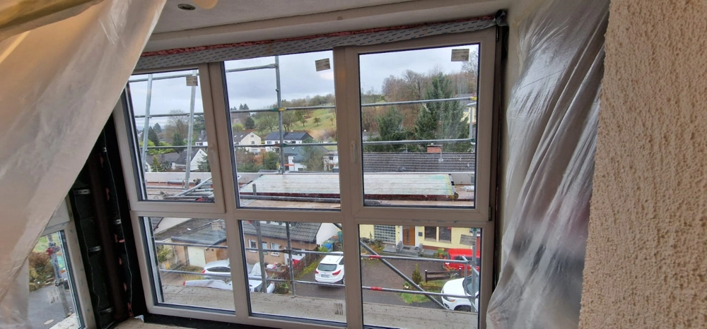 Fenstermontage eines mehrteiligen Kunststofffensters in Rohbau mit Schutzfolie und Gerüst