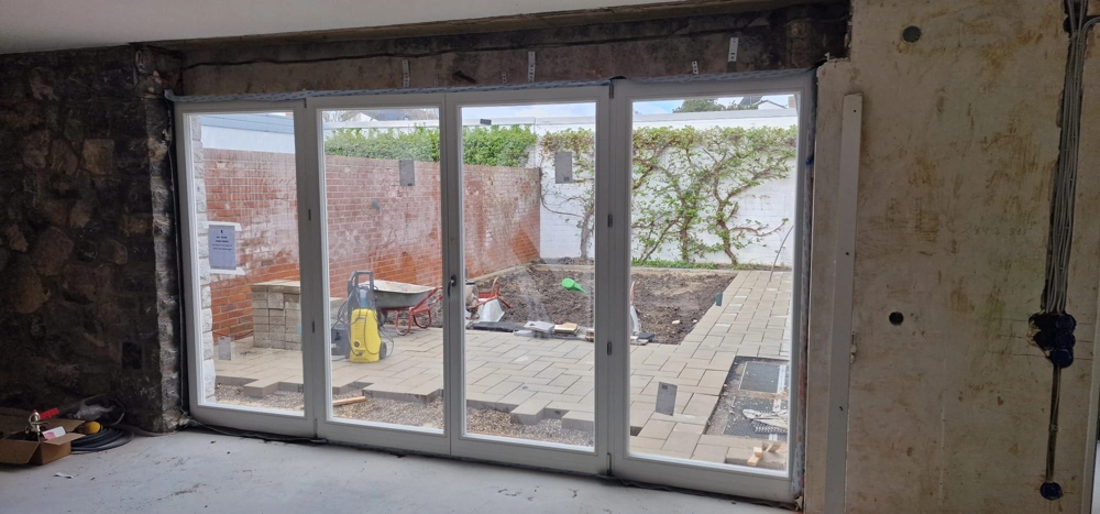Innenansicht einer großen weißen mehrteiligen Kunststoff-Schiebetür zur Terrasse mit Pflasterarbeiten im Außenbereich, Fenstermontage