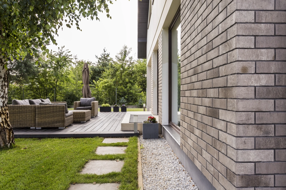 Klinkerfassaden an moderner Hausecke mit Terrassendielen, Gartenmöbeln und gepflegtem Rasen