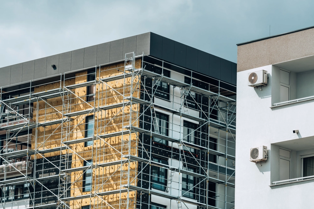 Gerüst vor mehrgeschossiger Fassade mit Dämmplatten und Fenstermontage im Rahmen einer Fassadensanierung