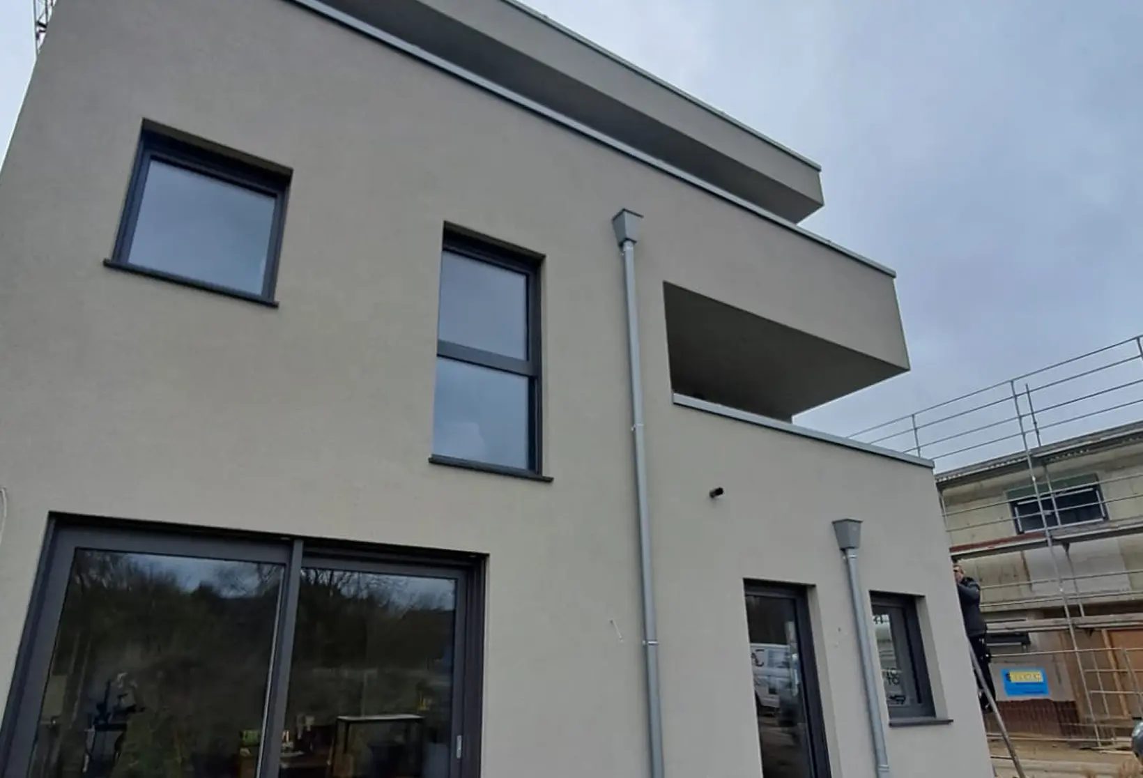 Moderne zweistöckige Fassade mit großen Fenstern, Balkon und frischem Außenputz Fassadenbau