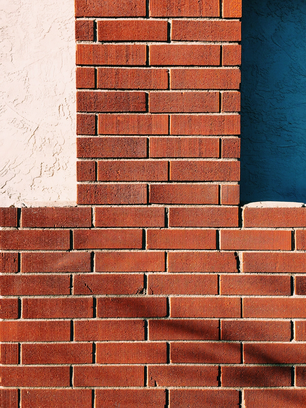 Rote Klinkerfassade mit weißem Putz links und blauem Putz rechts, vertikale Backsteinleiste